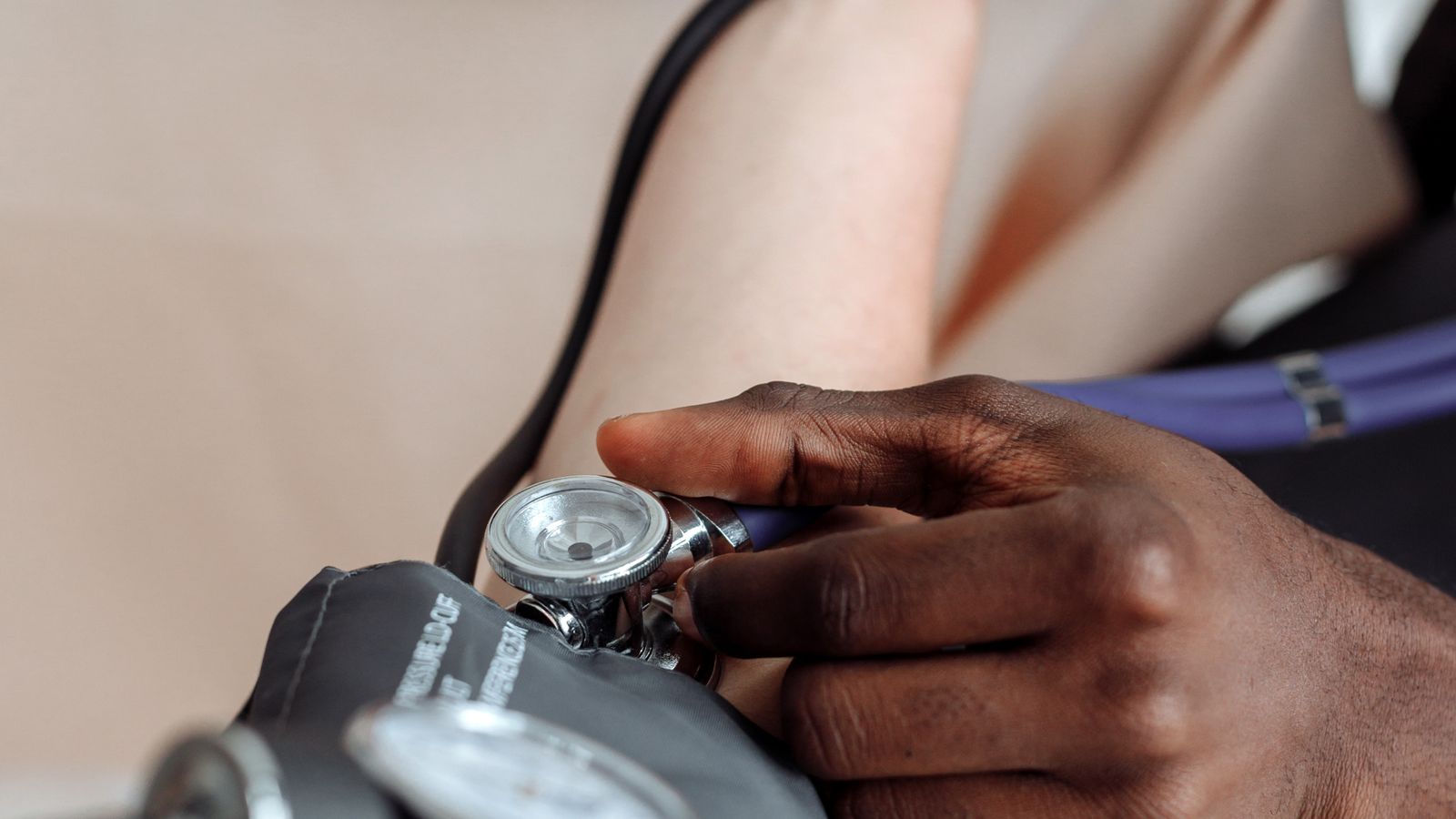 A clinician checking a blood pressure cuff and gauge on a patient's arm.