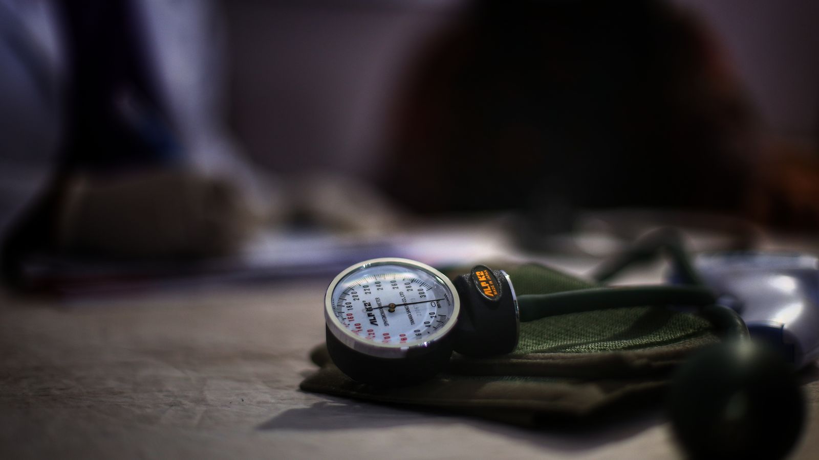 A manual blood pressure gauge, cuff and inflation bulb resting on a clinic table.