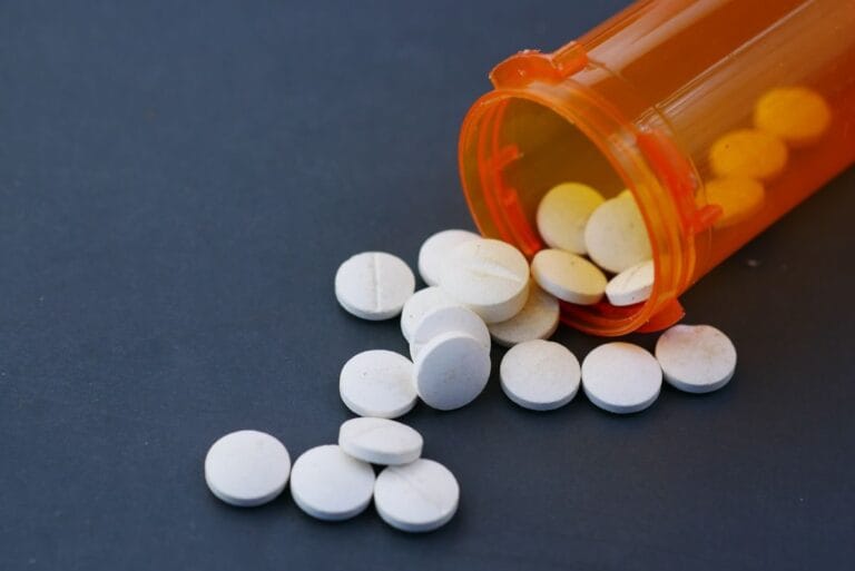 White tablets spilling from an orange prescription bottle, representing statin medication for cholesterol treatment.