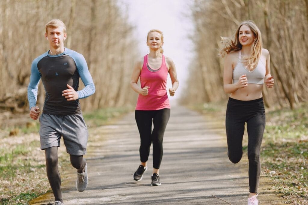 Three adults jogging together on a tree-lined park path.