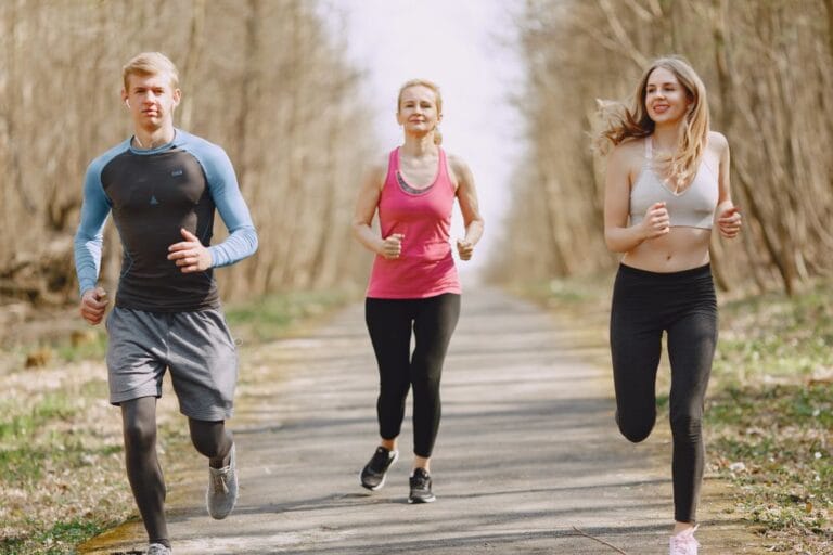 Three adults jogging together on a tree-lined park path.