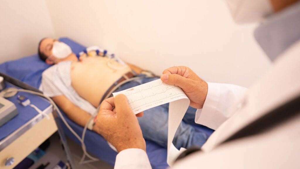 Clinician reviewing an ECG recording while a patient lies on an examination couch.